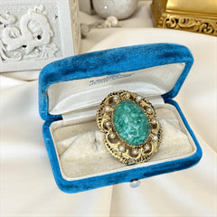 Vintage brooch pendant with mottled green glass cabochon, faux pearls, and ornate gold tone filigree, photographed front and back to highlight its 1960s–70s revival style and dual-wear functionality.