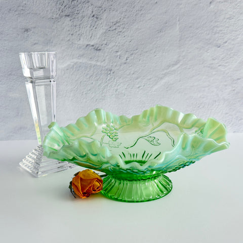 Antique green opalescent glass compote bowl with a ruffled rim, grape and leaf pattern, and a round pedestal foot, photographed against a light background.