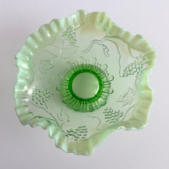 Antique green opalescent glass compote bowl with a ruffled rim, grape and leaf pattern, and a round pedestal foot, photographed against a light background.