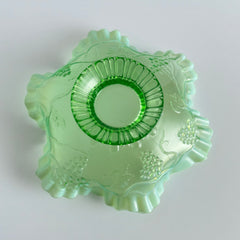Antique green opalescent glass compote bowl with a ruffled rim, grape and leaf pattern, and a round pedestal foot, photographed against a light background.