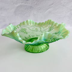 Antique green opalescent glass compote bowl with a ruffled rim, grape and leaf pattern, and a round pedestal foot, photographed against a light background.