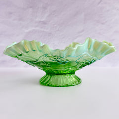 Antique green opalescent glass compote bowl with a ruffled rim, grape and leaf pattern, and a round pedestal foot, photographed against a light background.