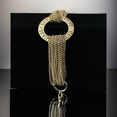 Gold tone Guess bracelet with multi-strand chains and a central ring engraved with ‘GUESS’ and accented by clear rhinestones, shown on neutral backdrop.