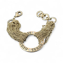Gold tone Guess bracelet with multi-strand chains and a central ring engraved with ‘GUESS’ and accented by clear rhinestones, shown on neutral backdrop.