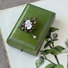 Vintage white guilloché enamel brooch with pink rose motif, faux pearls, and ornate antiqued gold tone filigree frame with teardrop pearl accent.