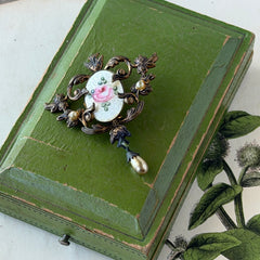 Vintage white guilloché enamel brooch with pink rose motif, faux pearls, and ornate antiqued gold tone filigree frame with teardrop pearl accent.