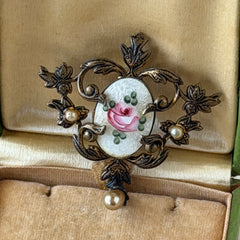 Vintage white guilloché enamel brooch with pink rose motif, faux pearls, and ornate antiqued gold tone filigree frame with teardrop pearl accent.