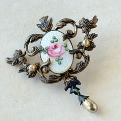 Vintage white guilloché enamel brooch with pink rose motif, faux pearls, and ornate antiqued gold tone filigree frame with teardrop pearl accent.