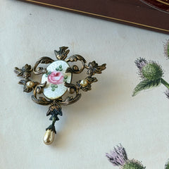 Vintage white guilloché enamel brooch with pink rose motif, faux pearls, and ornate antiqued gold tone filigree frame with teardrop pearl accent.