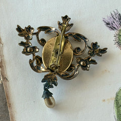 Vintage white guilloché enamel brooch with pink rose motif, faux pearls, and ornate antiqued gold tone filigree frame with teardrop pearl accent.