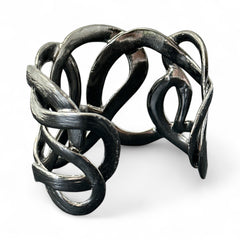 Textured dark silver tone cuff bracelet with interwoven, ribbon-like bands forming a sculptural openwork design; hammered finish adds depth and dimension to the modern, unsigned piece.