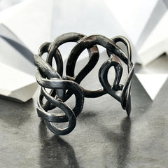 Textured dark silver tone cuff bracelet with interwoven, ribbon-like bands forming a sculptural openwork design; hammered finish adds depth and dimension to the modern, unsigned piece.