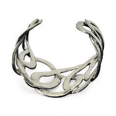 Textured dark silver tone cuff bracelet with interwoven, ribbon-like bands forming a sculptural openwork design; hammered finish adds depth and dimension to the modern, unsigned piece.