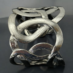 Textured dark silver tone cuff bracelet with interwoven, ribbon-like bands forming a sculptural openwork design; hammered finish adds depth and dimension to the modern, unsigned piece.