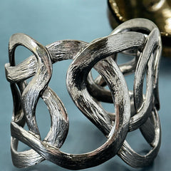 Textured dark silver tone cuff bracelet with interwoven, ribbon-like bands forming a sculptural openwork design; hammered finish adds depth and dimension to the modern, unsigned piece.