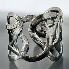 Textured dark silver tone cuff bracelet with interwoven, ribbon-like bands forming a sculptural openwork design; hammered finish adds depth and dimension to the modern, unsigned piece.