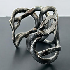 Textured dark silver tone cuff bracelet with interwoven, ribbon-like bands forming a sculptural openwork design; hammered finish adds depth and dimension to the modern, unsigned piece.