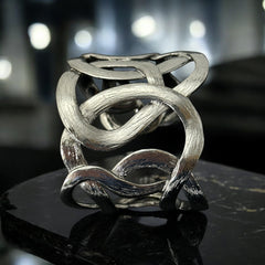 Textured dark silver tone cuff bracelet with interwoven, ribbon-like bands forming a sculptural openwork design; hammered finish adds depth and dimension to the modern, unsigned piece.