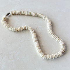 Vintage 1970s Hawaiian puka shell necklace made of natural white‑cream shells, shown coiled on a neutral background.