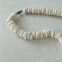 Vintage 1970s Hawaiian puka shell necklace made of natural white‑cream shells, shown coiled on a neutral background.