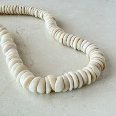 Vintage 1970s Hawaiian puka shell necklace made of natural white‑cream shells, shown coiled on a neutral background.