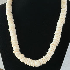 Vintage 1970s Hawaiian puka shell necklace made of natural white‑cream shells, shown coiled on a neutral background.