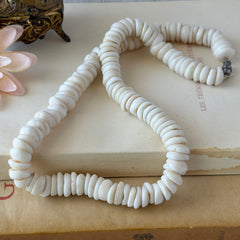 Vintage 1970s Hawaiian puka shell necklace made of natural white‑cream shells, shown coiled on a neutral background.