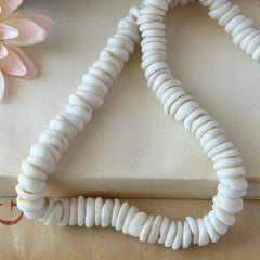Vintage 1970s Hawaiian puka shell necklace made of natural white‑cream shells, shown coiled on a neutral background.