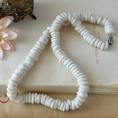 Vintage 1970s Hawaiian puka shell necklace made of natural white‑cream shells, shown coiled on a neutral background.