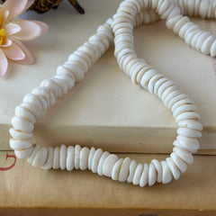 Vintage 1970s Hawaiian puka shell necklace made of natural white‑cream shells, shown coiled on a neutral background.