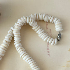 Vintage 1970s Hawaiian puka shell necklace made of natural white‑cream shells, shown coiled on a neutral background.
