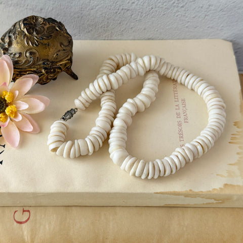 Vintage 1970s Hawaiian puka shell necklace made of natural white‑cream shells, shown coiled on a neutral background.