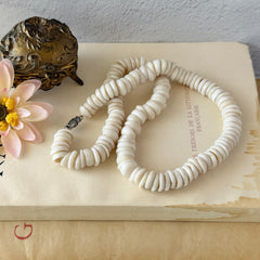 Vintage 1970s Hawaiian puka shell necklace made of natural white‑cream shells, shown coiled on a neutral background.