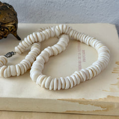 Vintage 1970s Hawaiian puka shell necklace made of natural white‑cream shells, shown coiled on a neutral background.