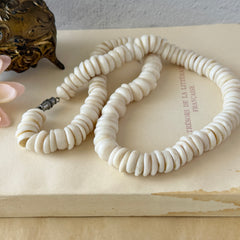 Vintage 1970s Hawaiian puka shell necklace made of natural white‑cream shells, shown coiled on a neutral background.