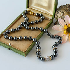 Vintage hematite bead necklace with gold‑tone and silver‑tone accents, hand‑knotted with slide ball clasp, displayed on green box.