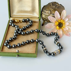 Vintage hematite bead necklace with gold‑tone and silver‑tone accents, hand‑knotted with slide ball clasp, displayed on green box.