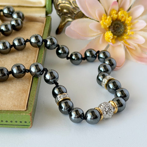 Vintage hematite bead necklace with gold‑tone and silver‑tone accents, hand‑knotted with slide ball clasp, displayed on green box.