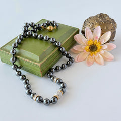 Vintage hematite bead necklace with gold‑tone and silver‑tone accents, hand‑knotted with slide ball clasp, displayed on green box.