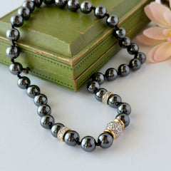 Vintage hematite bead necklace with gold‑tone and silver‑tone accents, hand‑knotted with slide ball clasp, displayed on green box.
