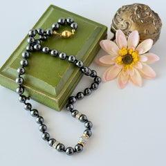 Vintage hematite bead necklace with gold‑tone and silver‑tone accents, hand‑knotted with slide ball clasp, displayed on green box.