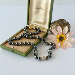 Vintage hematite bead necklace with gold‑tone and silver‑tone accents, hand‑knotted with slide ball clasp, displayed on green box.