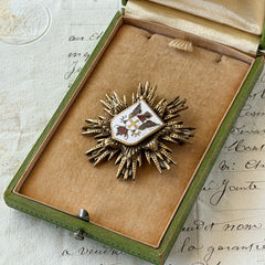Vintage gold‑tone heraldic brooch with white enamel shield and red‑gold griffin coat of arms, photographed on antique paper and boxes.