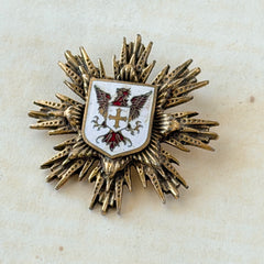 Vintage gold‑tone heraldic brooch with white enamel shield and red‑gold griffin coat of arms, photographed on antique paper and boxes.