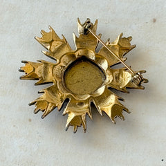 Vintage gold‑tone heraldic brooch with white enamel shield and red‑gold griffin coat of arms, photographed on antique paper and boxes.