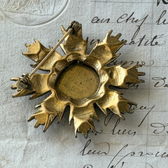 Vintage gold‑tone heraldic brooch with white enamel shield and red‑gold griffin coat of arms, photographed on antique paper and boxes.