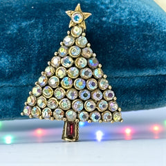 Vintage Hollycraft Christmas tree brooch with clear Aurora Borealis rhinestones in a gold-tone setting, featuring a gold star at the top and a red rhinestone base. Signed on the reverse and measuring approximately 1 3/8 inches tall by 1 inch wide.