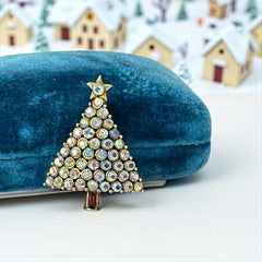 Vintage Hollycraft Christmas tree brooch with clear Aurora Borealis rhinestones in a gold-tone setting, featuring a gold star at the top and a red rhinestone base. Signed on the reverse and measuring approximately 1 3/8 inches tall by 1 inch wide.
