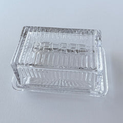 Vintage clear glass butter dish with raised “Beurre” lettering visible through the lid and ribbed radiating base.