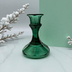 Pair of vintage Indiana Glass green candlestick holders with hexagonal bases, shown on a white surface. The emerald green glass catches the light, highlighting their faceted mid-century design and tapered silhouette. Ideal for holiday styling or eco-conscious vintage decor.